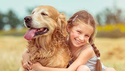 Smiling girl with braided hair hugs a happy golden retriever outside an Idaho pizza restaurant.