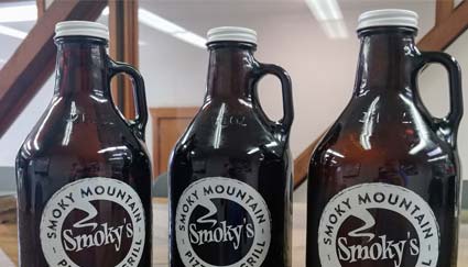 Three brown Smoky Mountain Pizzeria Grill growlers with white labels, side by side on a table.