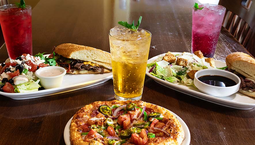 Pizza, salads, and sandwiches from Smoky Mountain Pizzeria Grill on a wooden table in the banquet room.