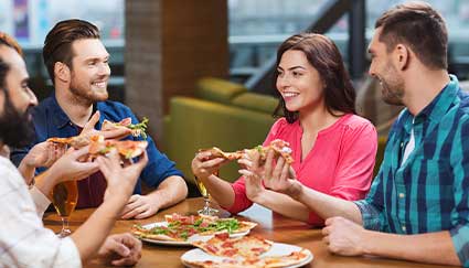 Four friends enjoy Idaho pizza together, smiling in a cozy, casual restaurant setting.