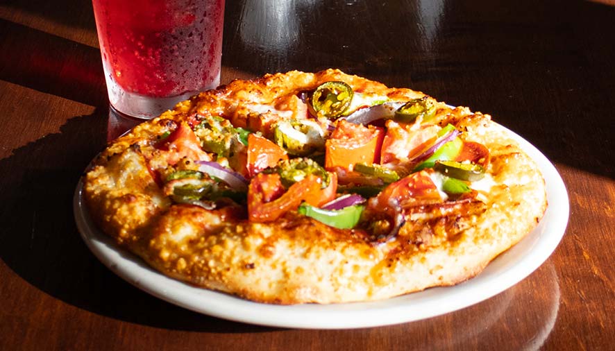 A veggie pizza with peppers and onions at our Idaho restaurant, served beside a red drink.