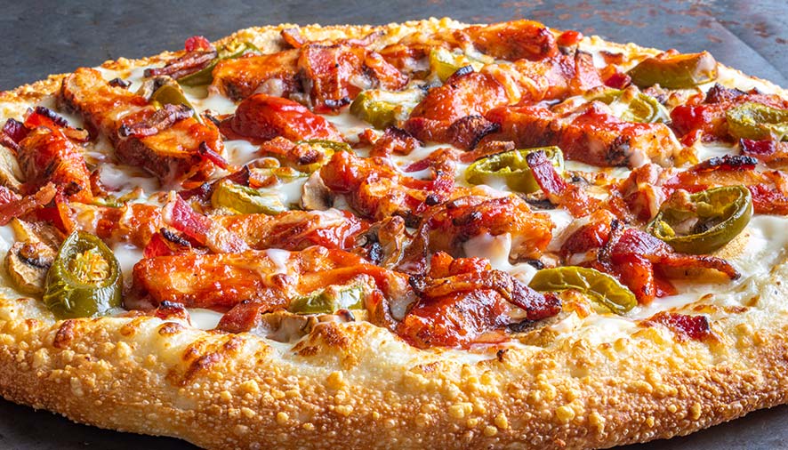 Close-up of a restaurant pizza topped with chicken, jalapeños, bacon, cheese, and golden crust.