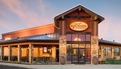 Exterior view of a Great Mountain Pizza restaurant at sunset, with large windows and lights.