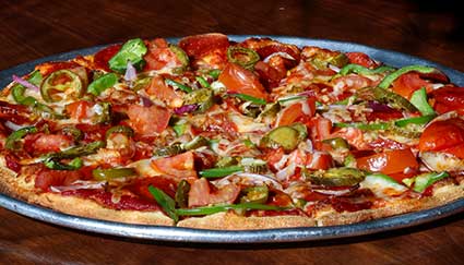 A loaded Idaho pizza topped with peppers, tomatoes, and pepperoni on a metal tray.