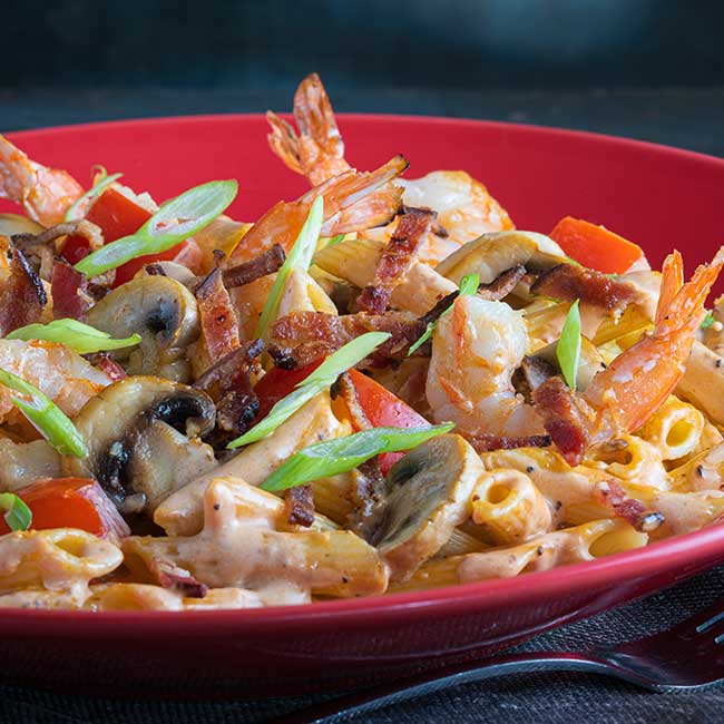 Pasta with shrimp, mushrooms, and bacon in a red bowl served in Boise, Idaho.