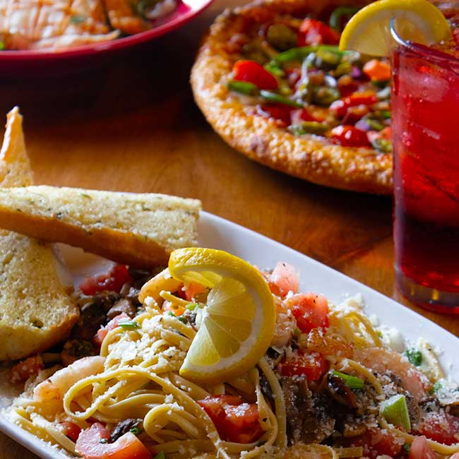 Plate of pasta with lemon, garlic bread, and pizza served in Boise Idaho on a wooden table.